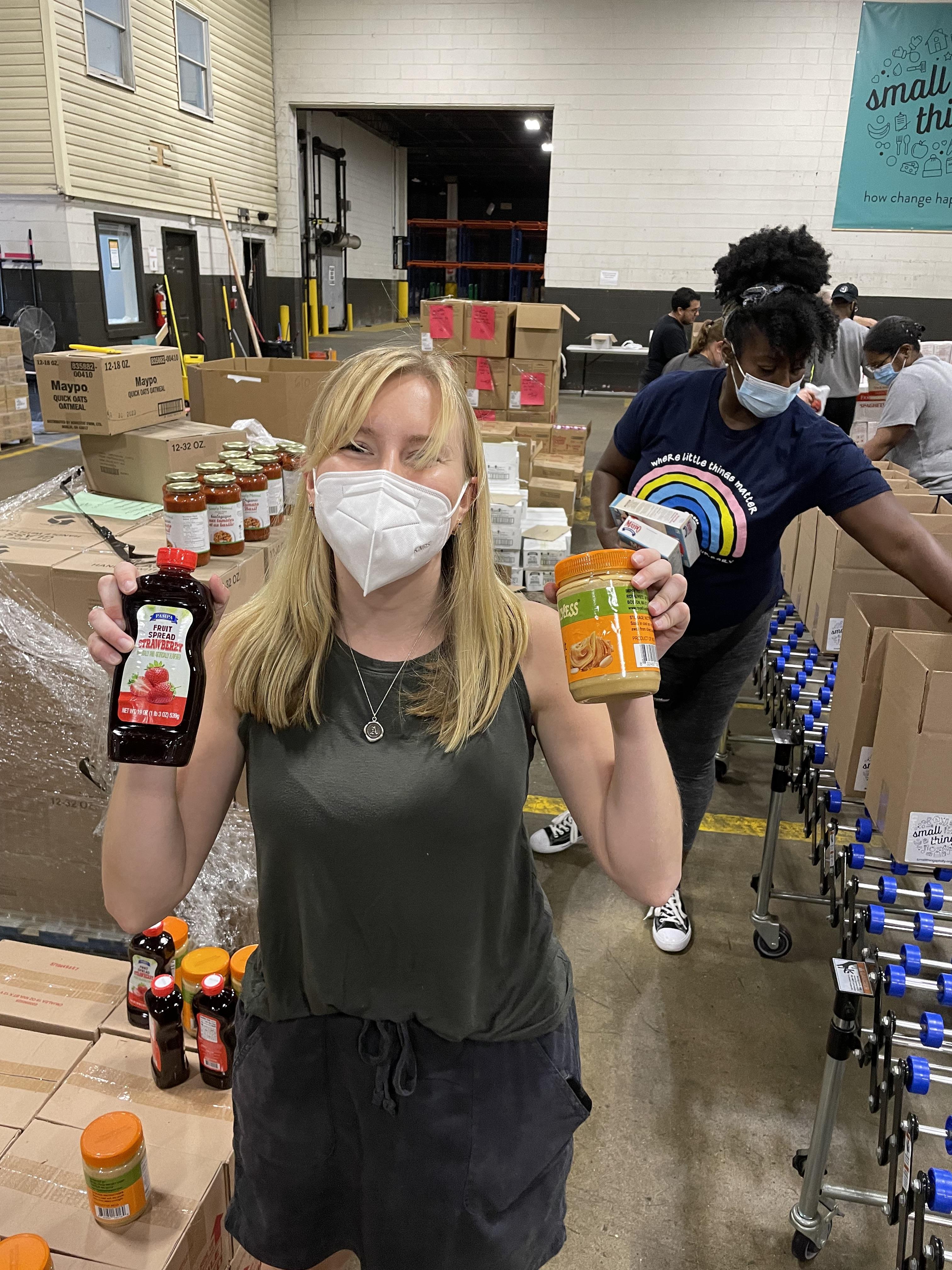 Woman in mask holding peanut butter and jelly at box packing event